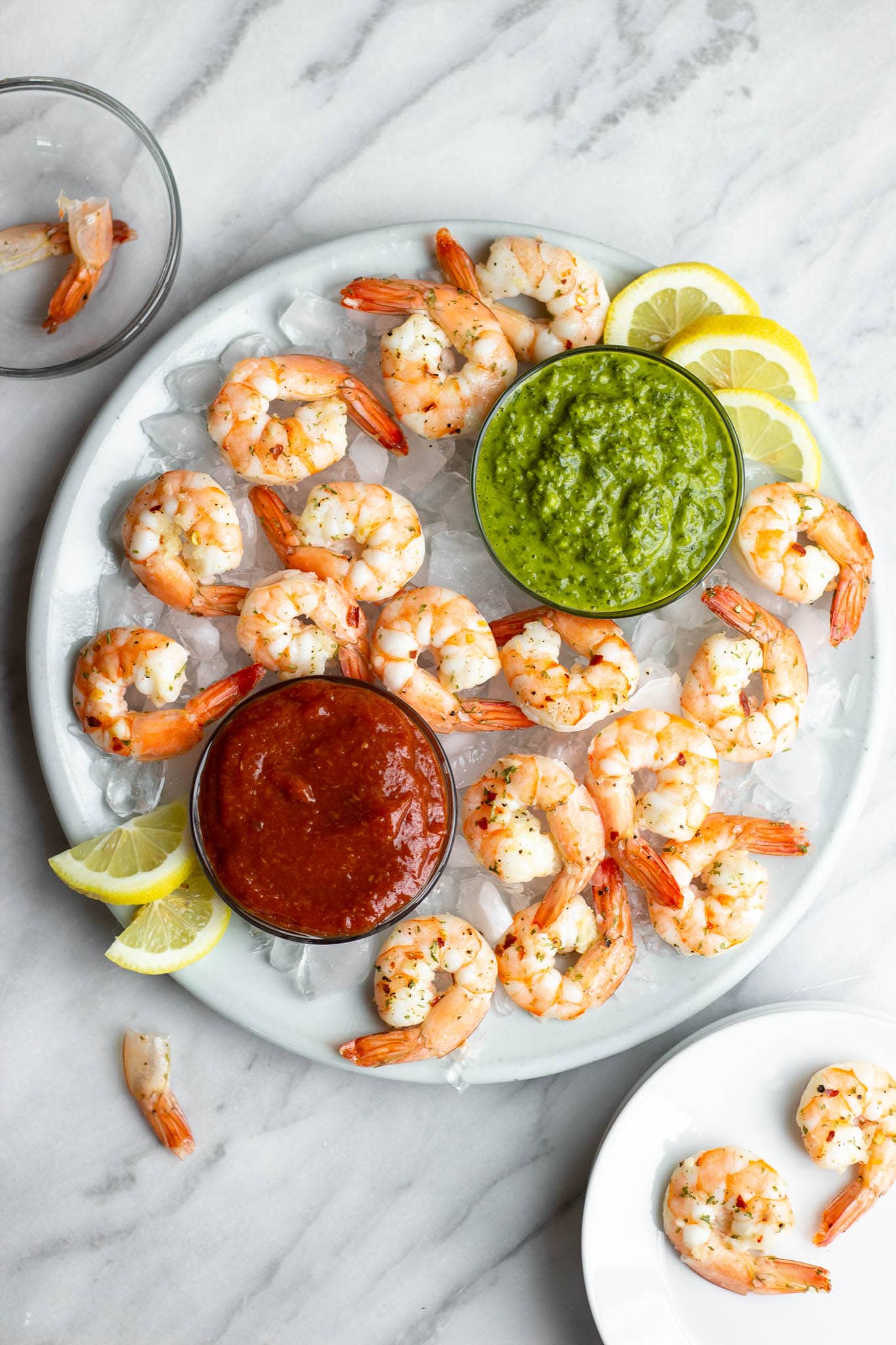 A platter of roasted shrimp cocktail with cocktail sauce and chimmichurri