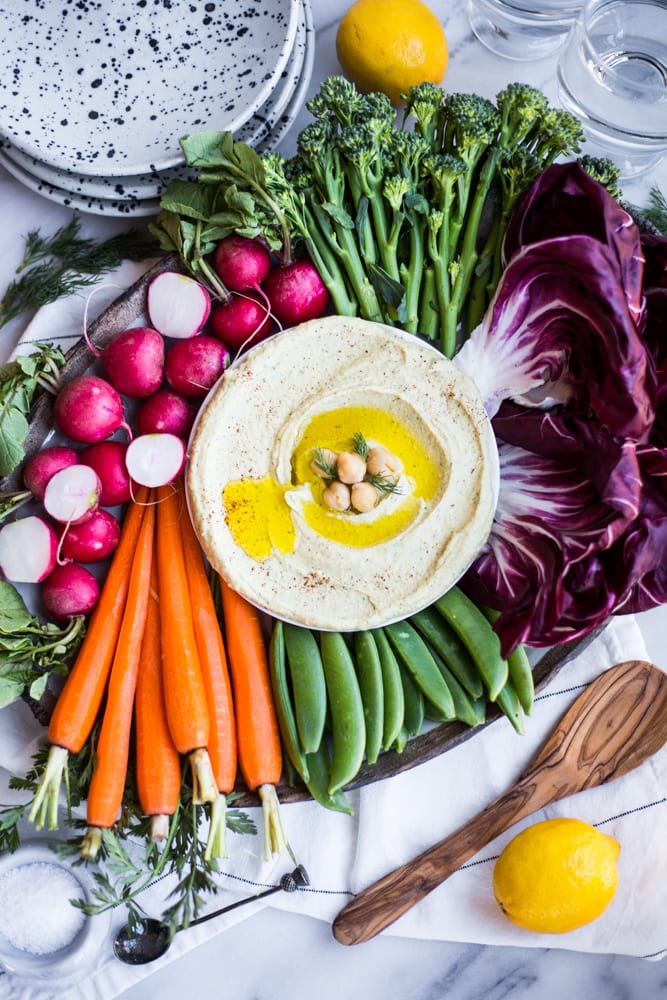 A platter filled with colorful vegetables and lemon dill hummus