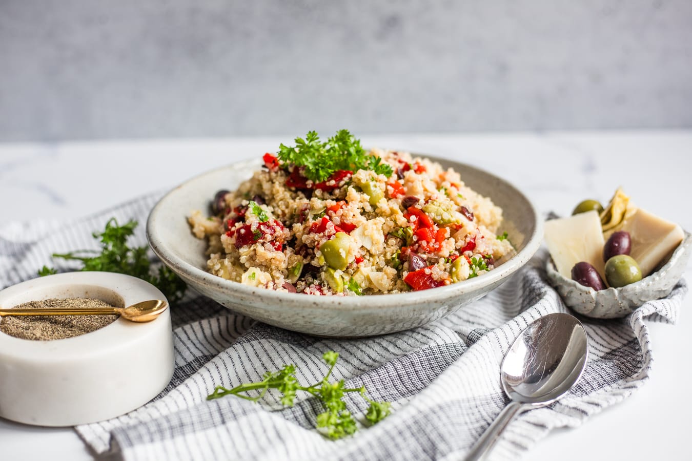 A bowl of quinoa mixed with roasted red peppers, parsley, olives, artichoke hearts, and hearts of palm