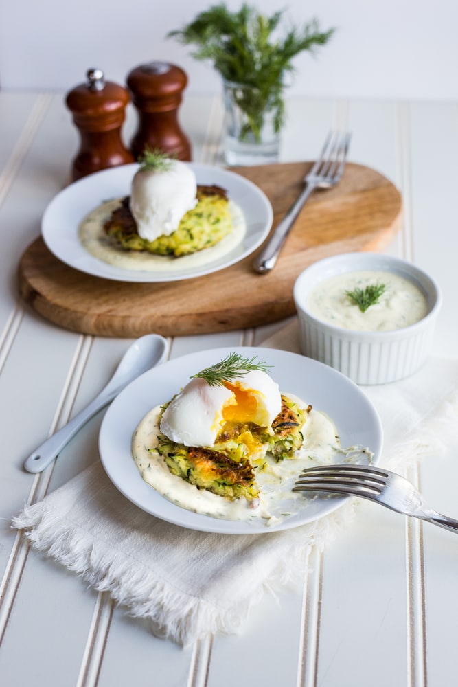 A poached egg cut open over a zucchini fritter with herbed greek yogurt hollandaise