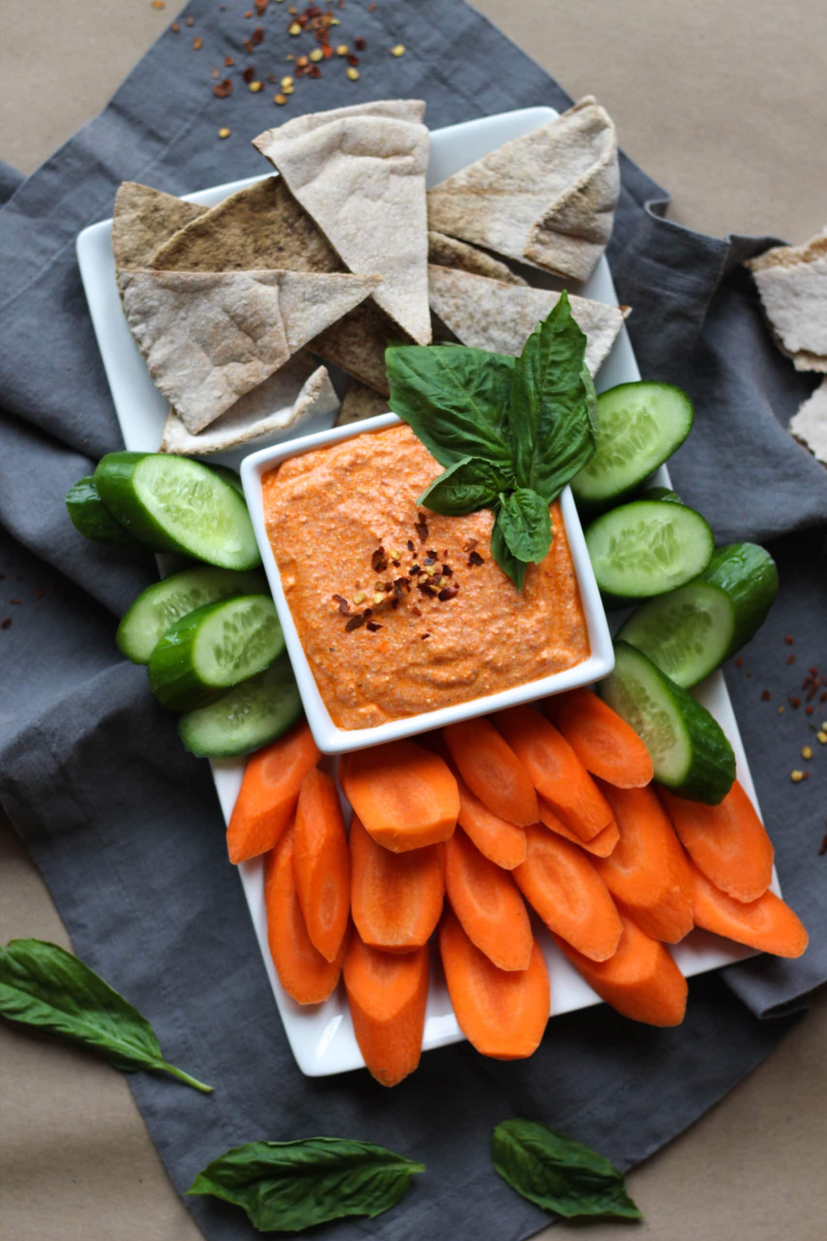 A platter of vegetables with a bowl of roasted red pepper feta dip