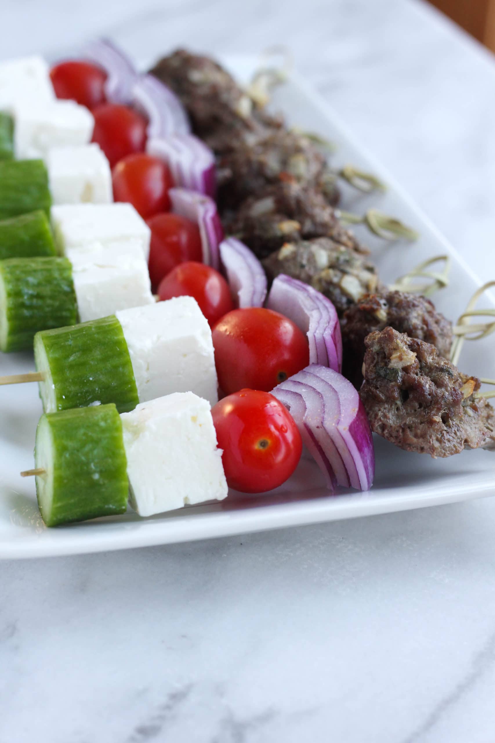Skewers of greek meatballs, red onion, feta cubes, cucumber, and tomatoes