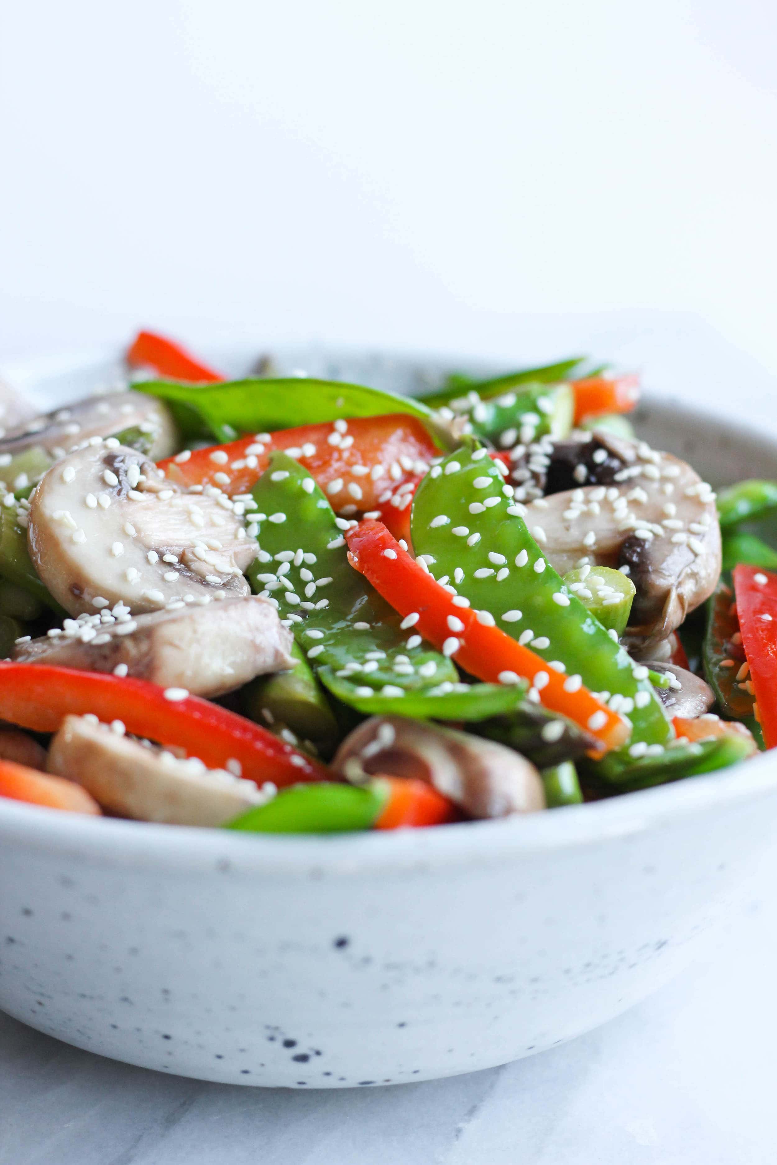 A bowl with red peppers, mushrooms, and pea pods topped with sesame seeds