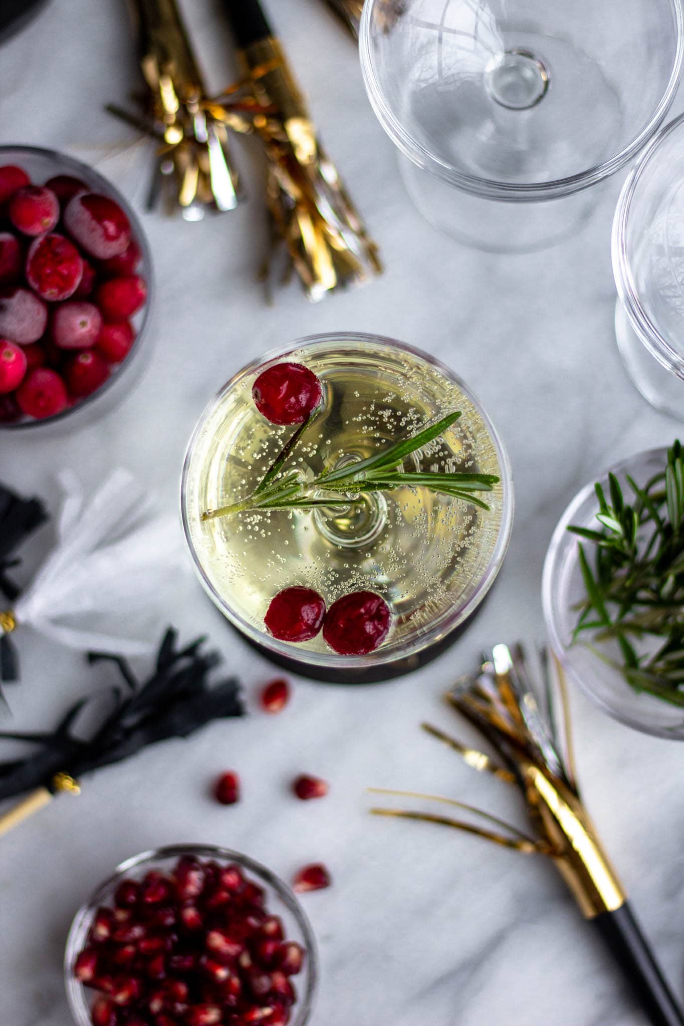 a glass of Prosecco with cranberries and rosemary