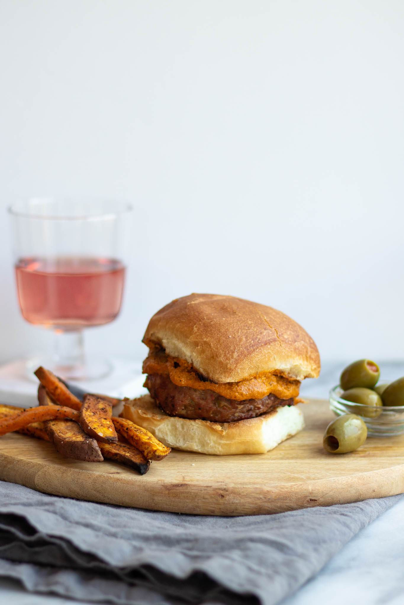 A Spanish Turkey burger on a platter with rosé wine, olives, and sweet potato fries