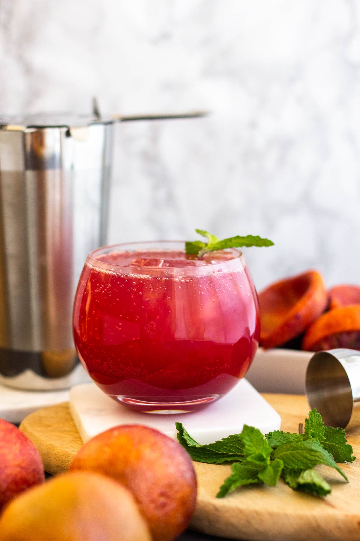 A ruby colored drink in a low ball glass surrounded by mint and blood oranges