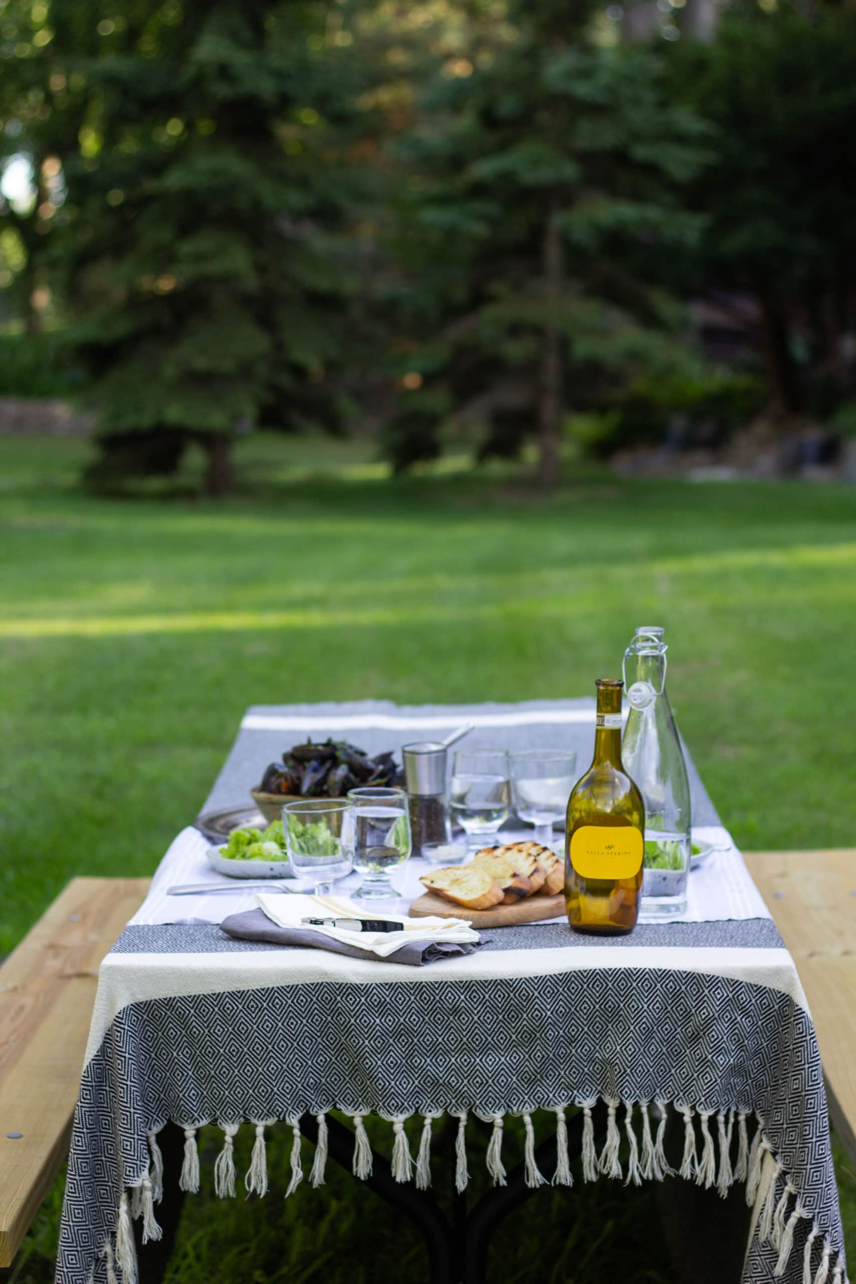 A picnic table set with serve ware, wine, and mussels