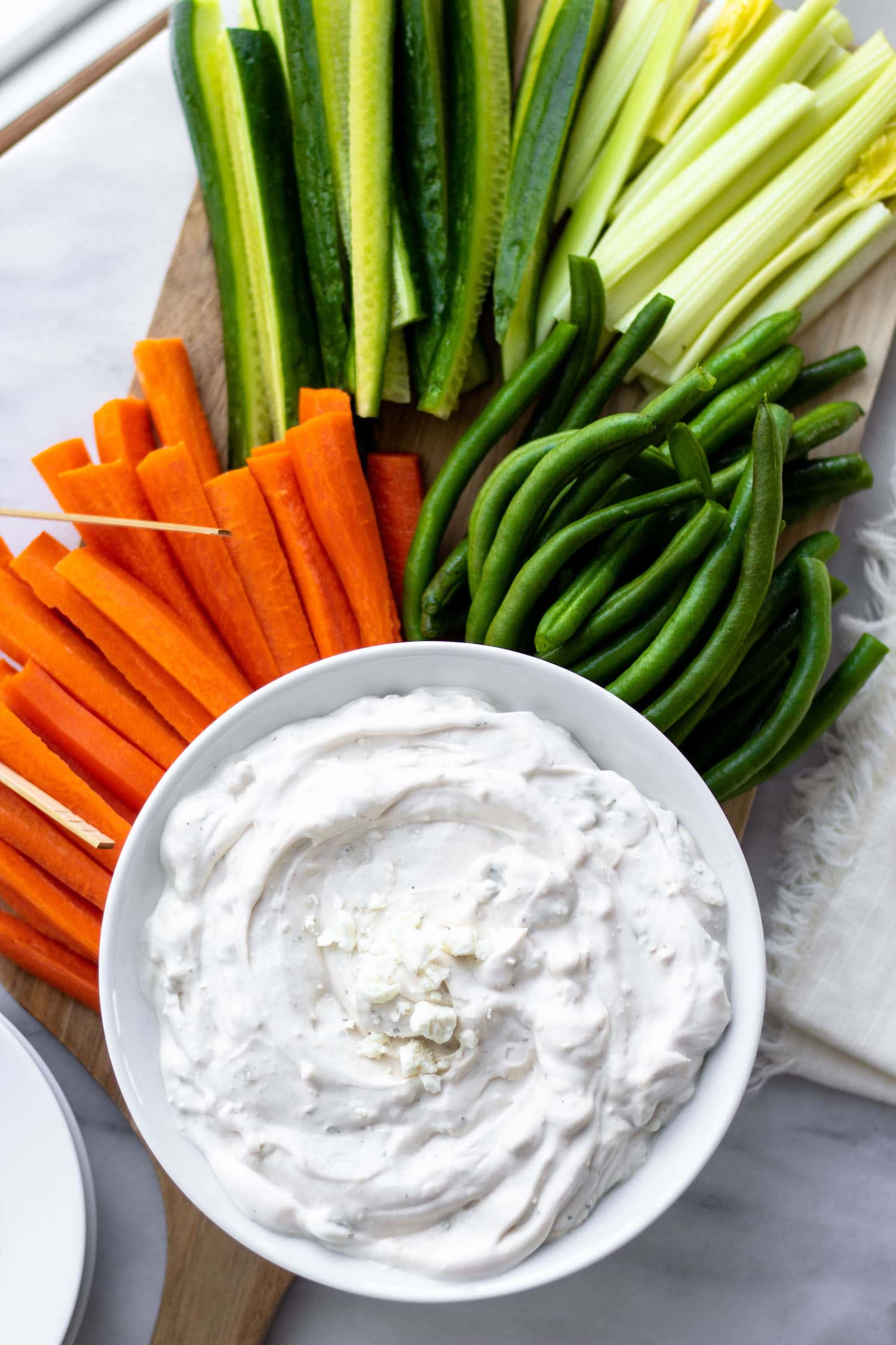 a bowl of Blue Cheese Dip surrounded by carrots, green beans, celery, and cucumber spears