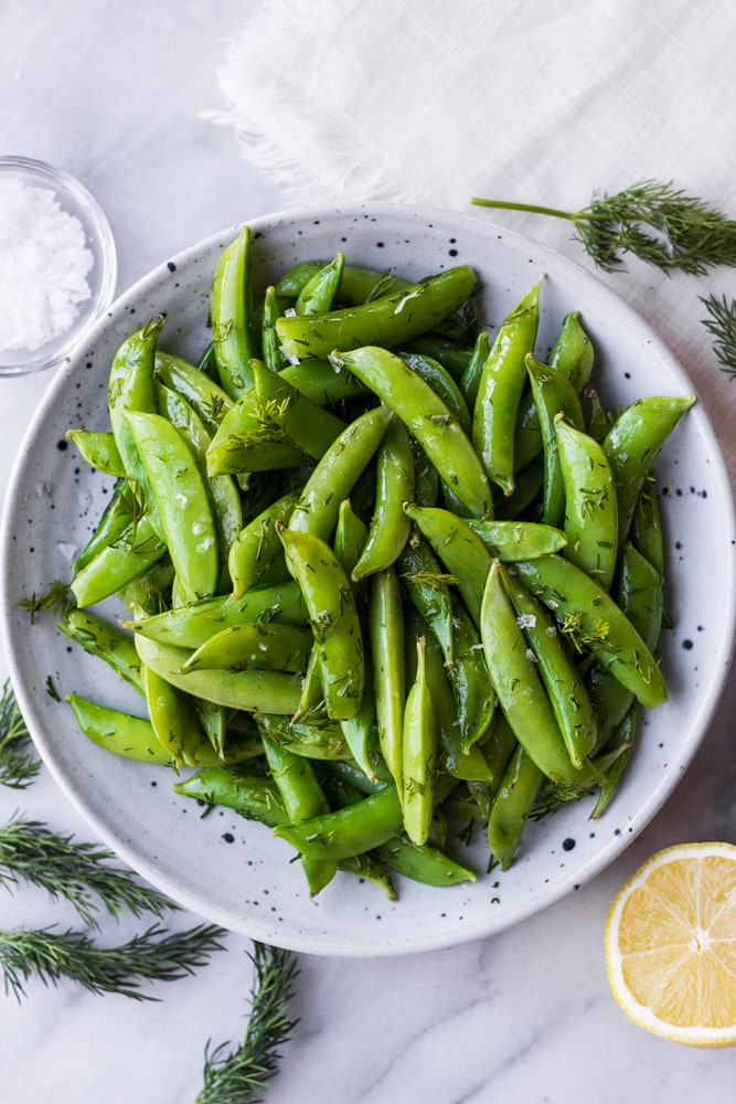 A plate filled with sautéed sugar snap peas topped with dill