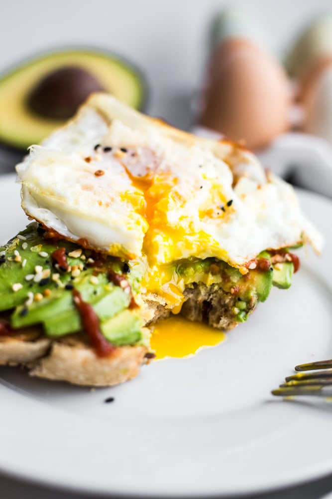 A fried egg with it's yolk dripping over avocado toast