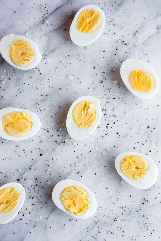 Halved hard boiled eggs on a marble tray with salt and pepper