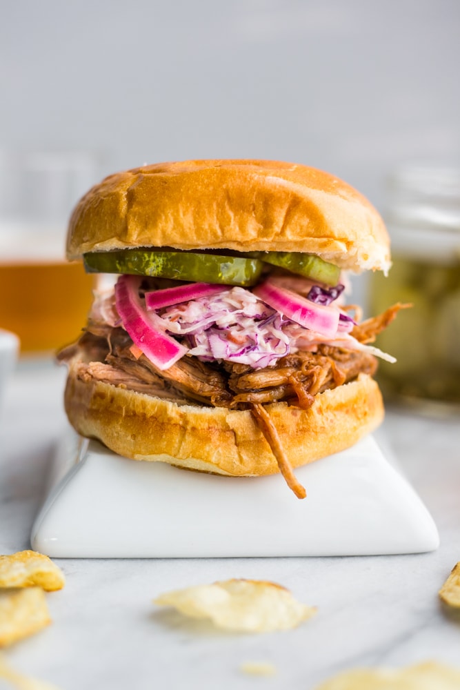 A barbecue pork sandwich topped with coleslaw, pickles, and pickles red onions