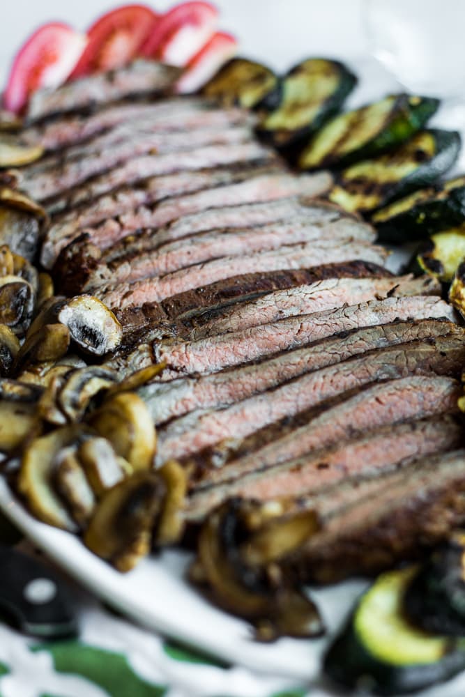 A platter of marinated flank steak surrounded by grilled vegetables