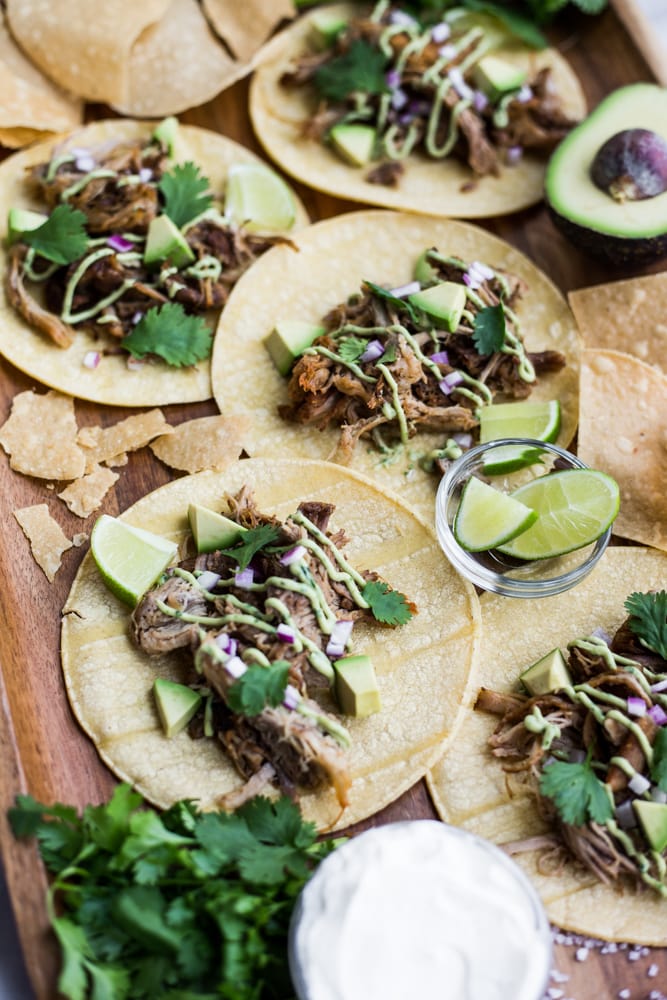 A platter of corn tortillas topped with shredded pork, cilantro, onion, and avocado crema
