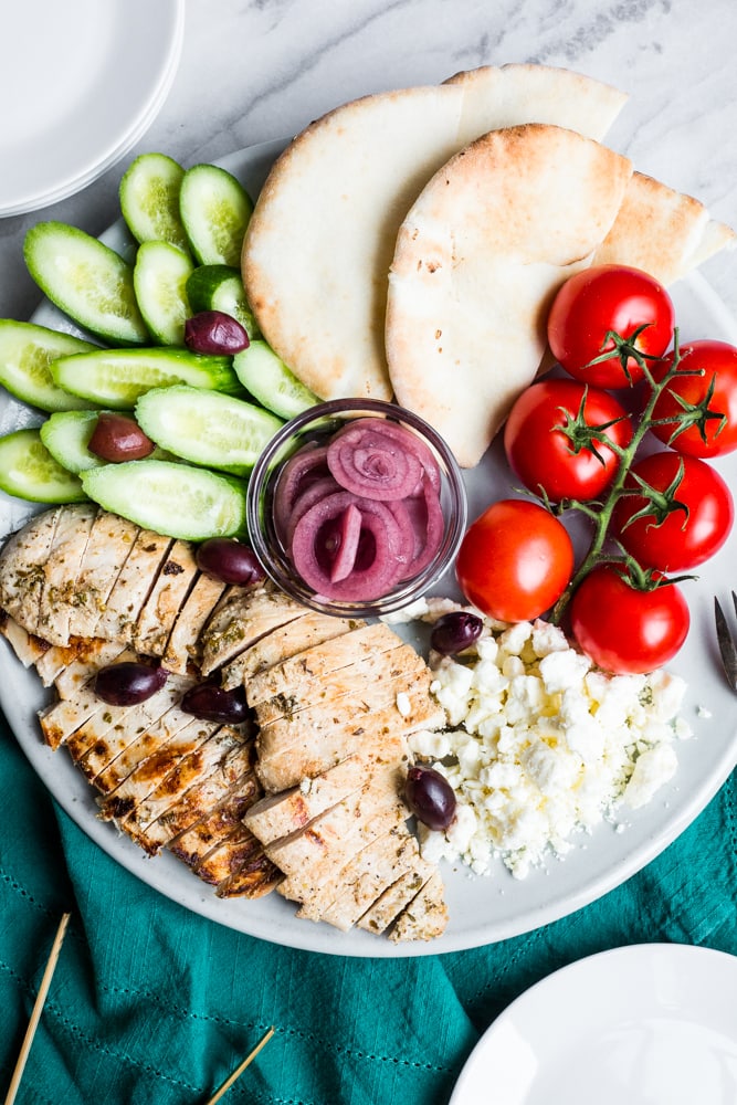 A platter of greek marinated chicken with cucumber, pita, tomatoes, olives, and feta