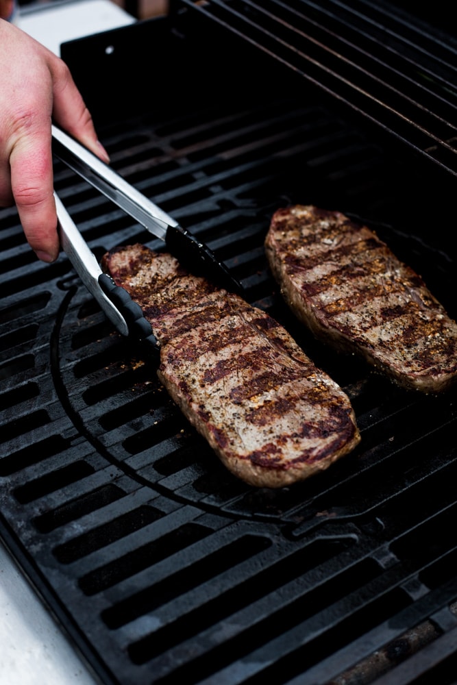 Two sirloin steaks on a grill being flipped with tongs