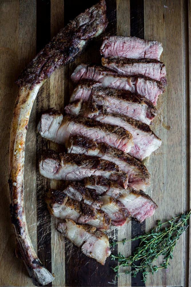A grilled tomahawk steak sliced and arranged next to its bone