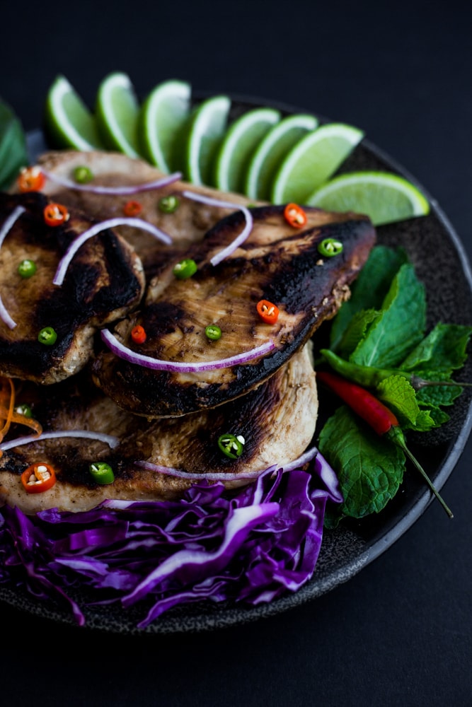 A platter of Sesame Ginger Chicken with carrots, purple cabbage, limes, and herbs surrounding it