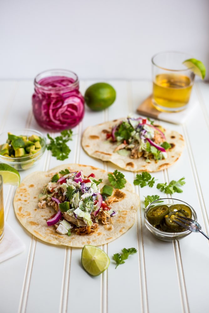 Fish tacos topped with dill slaw with a jar of pickled red onions and beer nearby