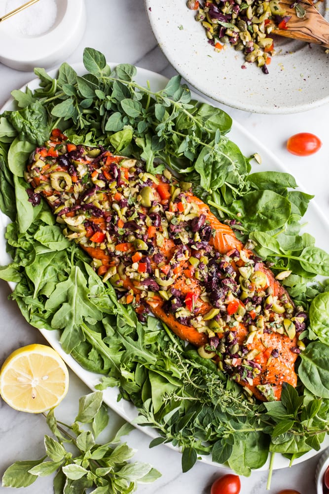 A platter with a salmon filet on a bed of greens topped with a colorful olive relish