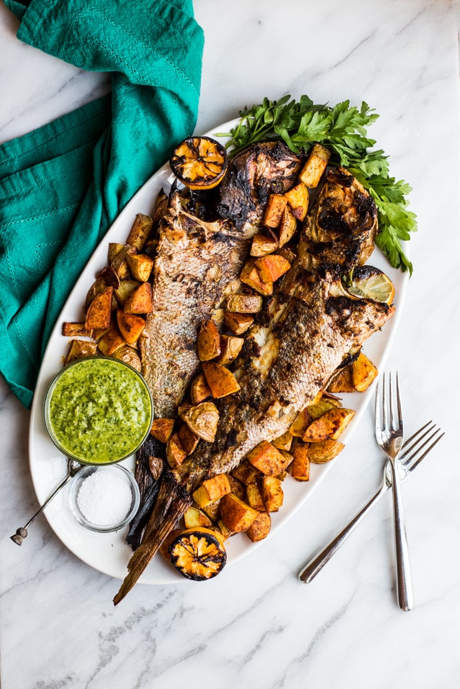 Whole grilled fish on a platter with chimmichurri and potatoes