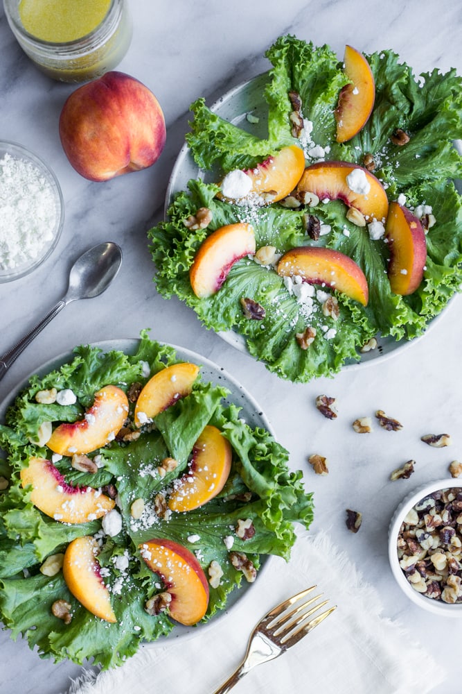 Two plates of salad topped with peaches, goat cheese, and walnuts