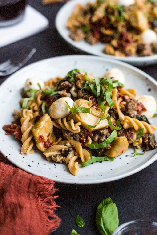 Two plates of pasta with cheese, sausage, basil, and sun-dried tomatoes
