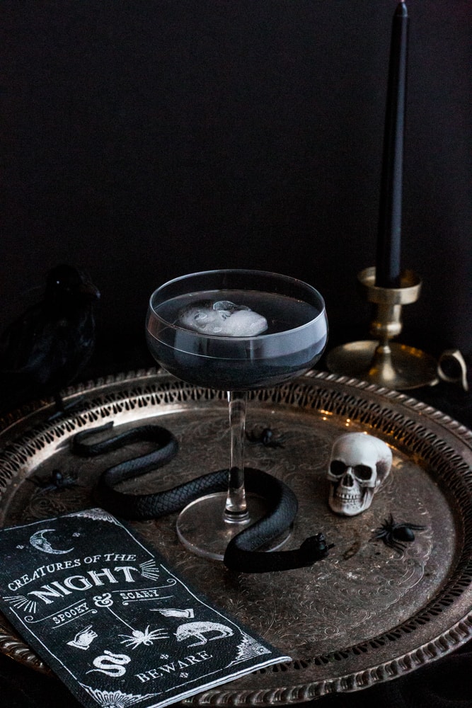 A coup filled with a black drink and a skull shaped ice cube