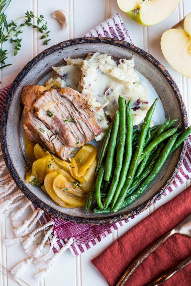 A plate filled with mashed potatoes, pork roast, apples, and green beans