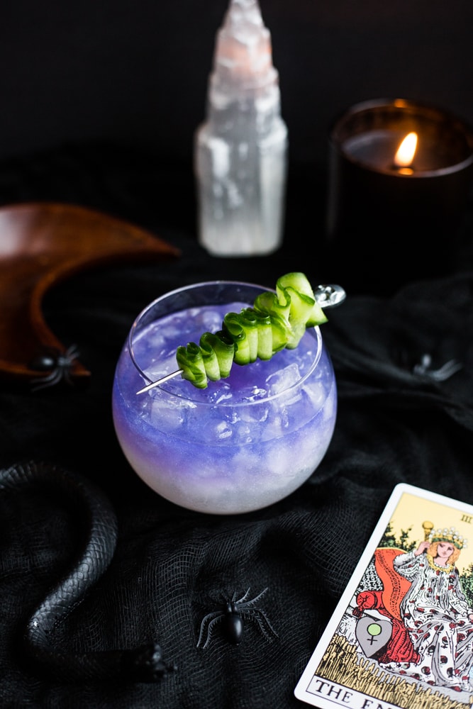 A two toned white and purple drink with a cucumber skewer