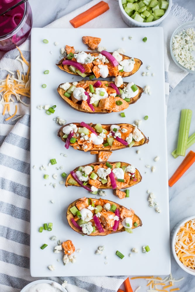 A platter of Buffalo Chicken Sweet Potato Skins topped with celery, pickled red onion, and blue cheese
