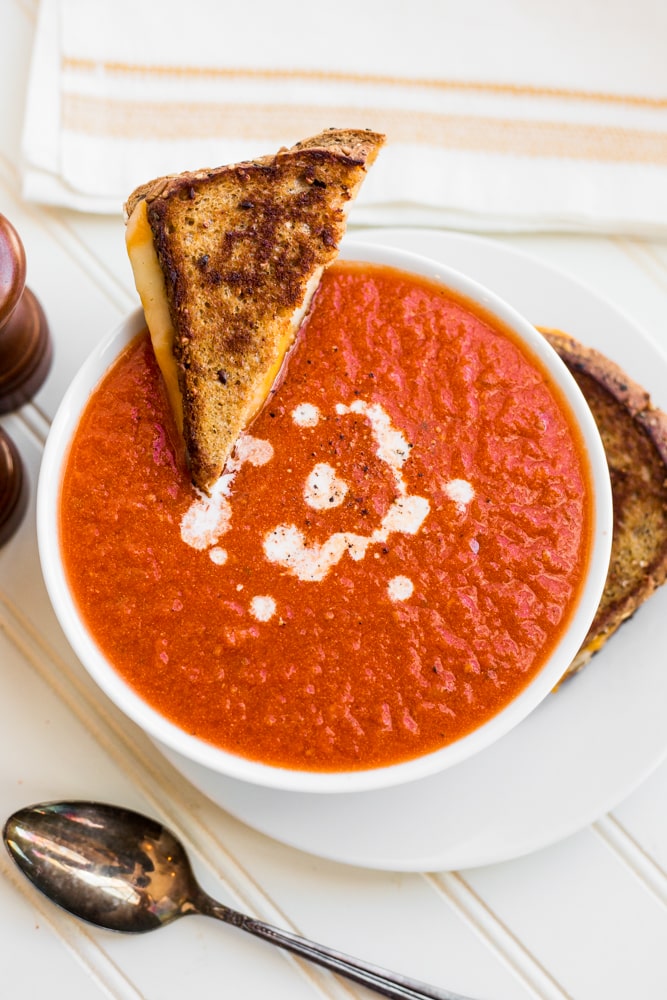 A bowl of easy creamy tomato soup with a halved grilled cheese sandwich