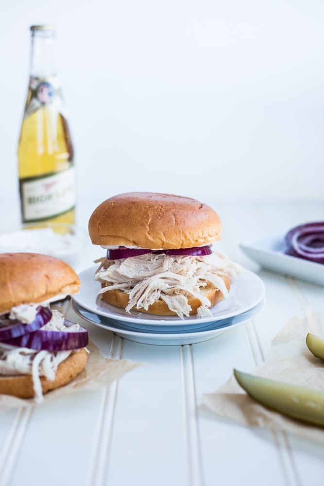 A slow cooker shredded turkey sandwich topped with red onion on a plate