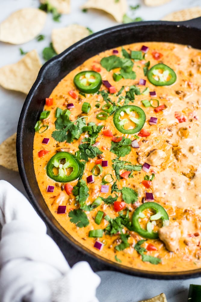 A cast iron skillet filled with the ultimate loaded queso topped with jalapeños, cilantro, red onion, and tomato