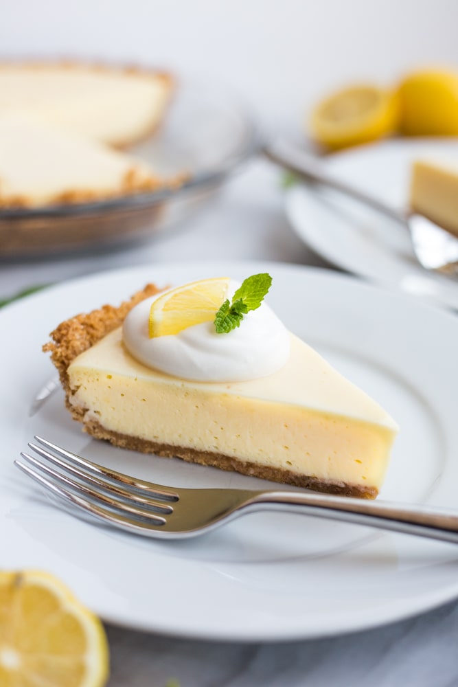A slice of lemon pie topped with whipped cream, a lemon slice, and a mint leaf