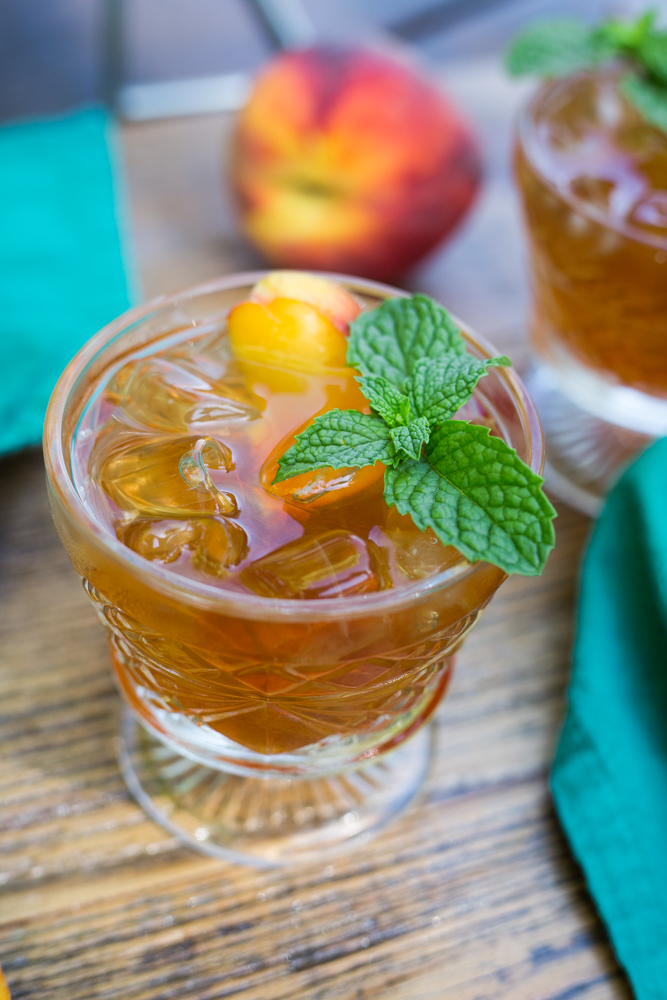 A glass of peach sun tea garnished with fresh mint and a peach slice