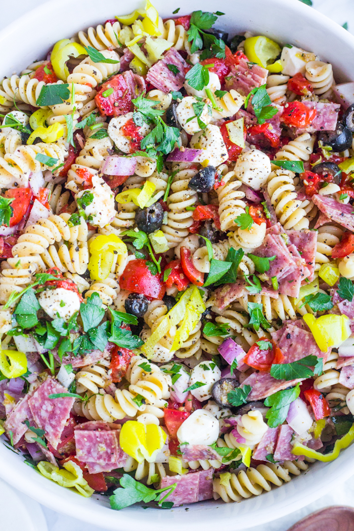 A bowl of Italian pasta salad with tomatoes, cheese, parsley, and salami