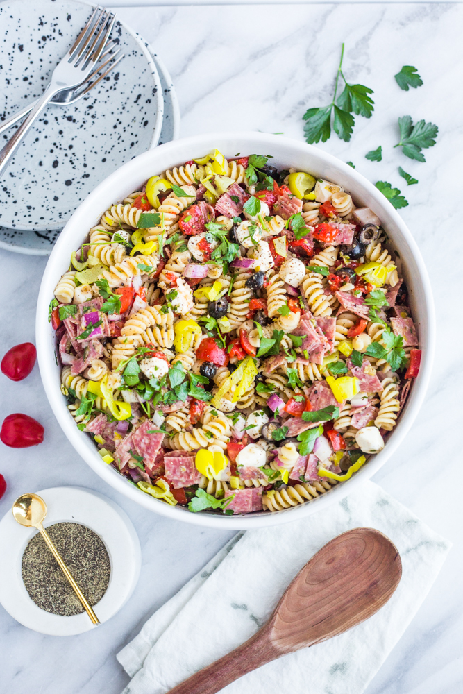 A bowl of Italian pasta salad with tomatoes, salami, and parsley