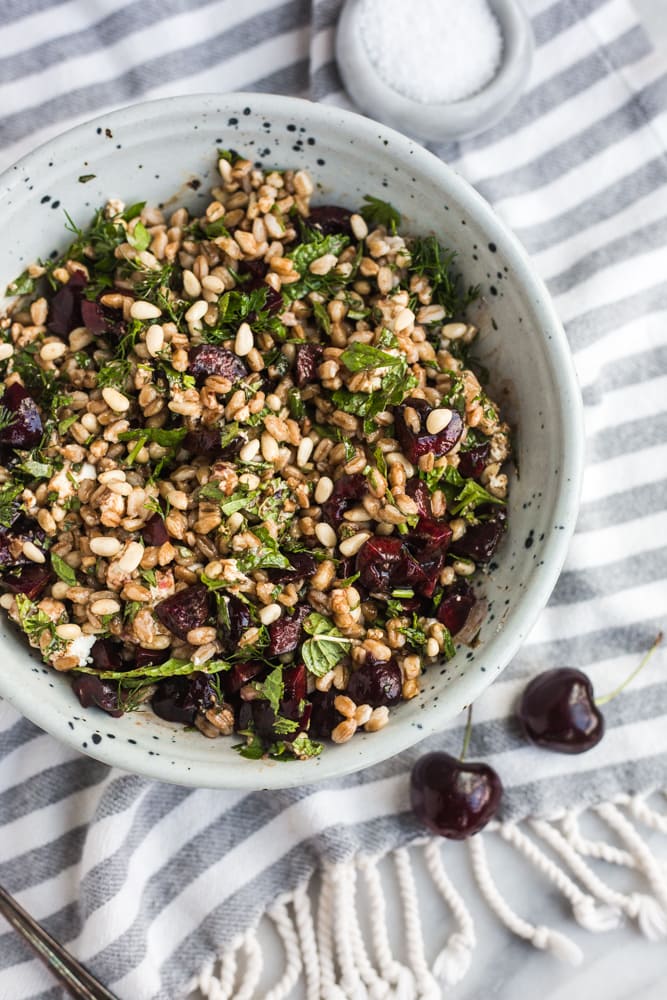 a bowl filled with a salad of farro, cherries, herbs, and goat cheese