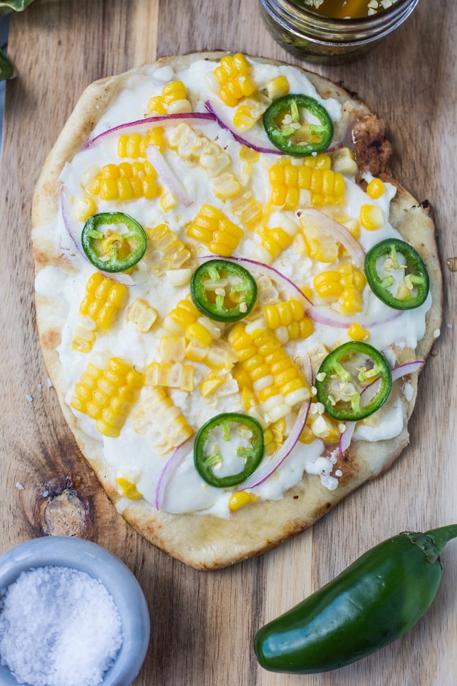 A when cutting board topped with a pizza with corn and jalapeños