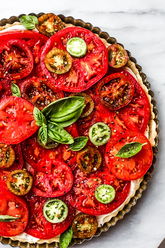 a tart topped with a variety of sliced tomatoes and basil leaves