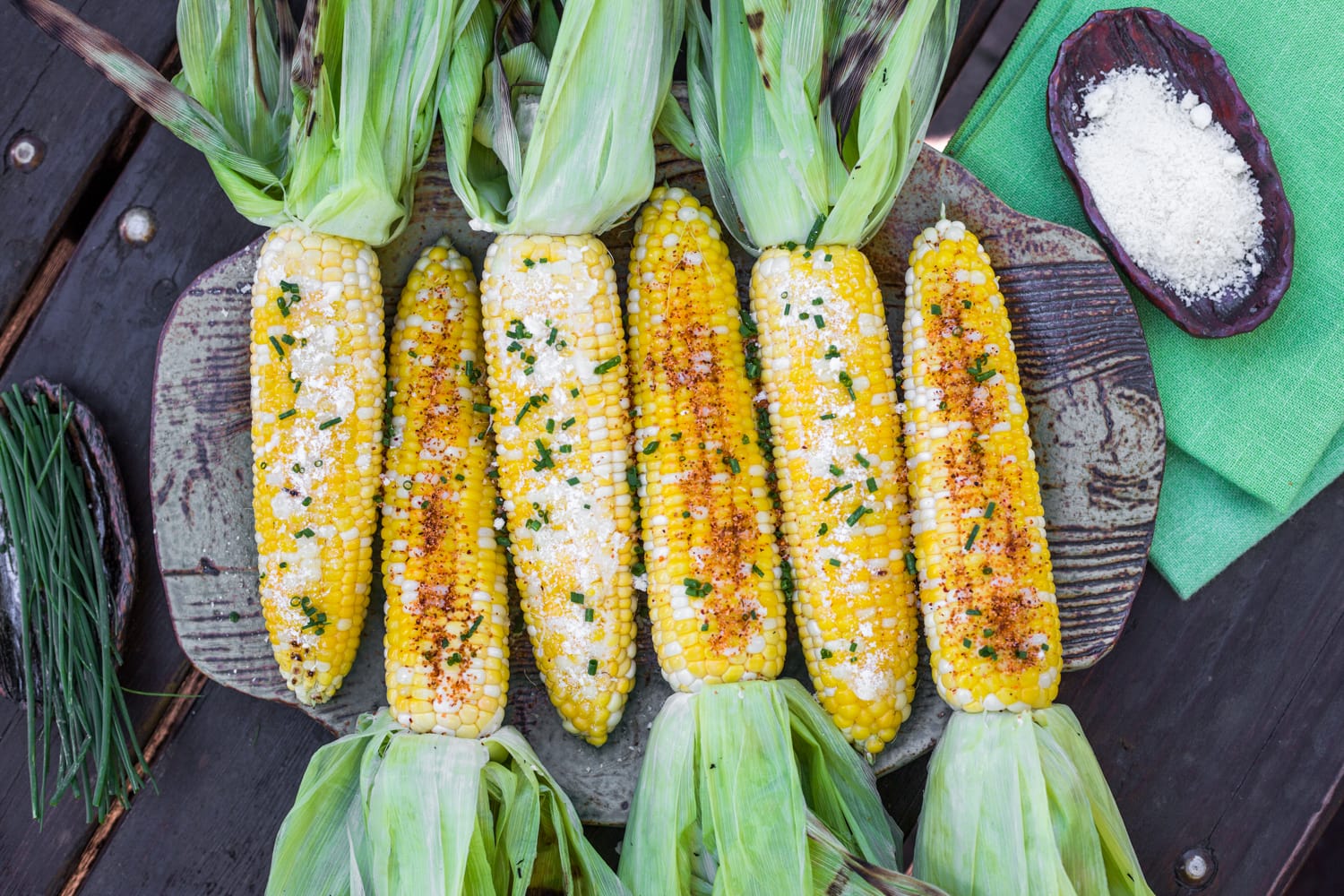 A platter of grilled corn on the cob topped with a variety of ingredients
