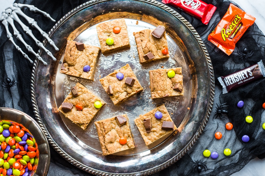 A silver platter topped with candy bar blondies topped with chocolate candies and purple, green, and orange M&Ms
