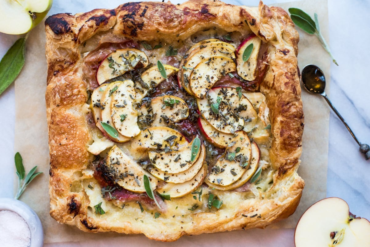 A puff pastry tart topped with apples, brie, and prosciutto