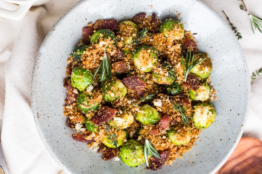 A bowl filled with Brussels sprouts topped with breadcrumbs and bacon