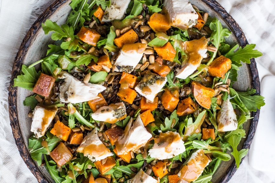 A plate topped with arugula, roasted sweet potatoes, wild rice, and turkey