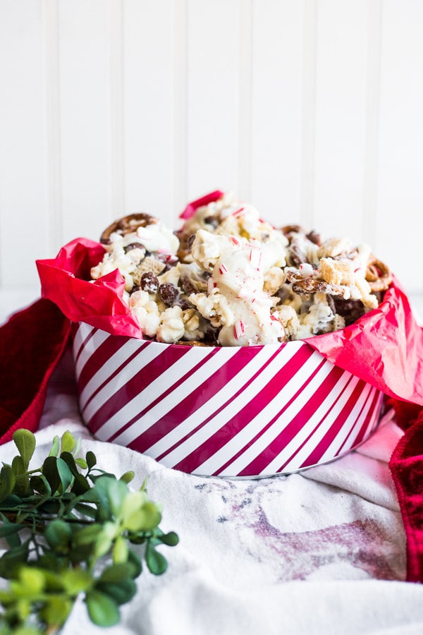 A white and red striped tin filled with red tissue paper and peppermint crunch snack mix
