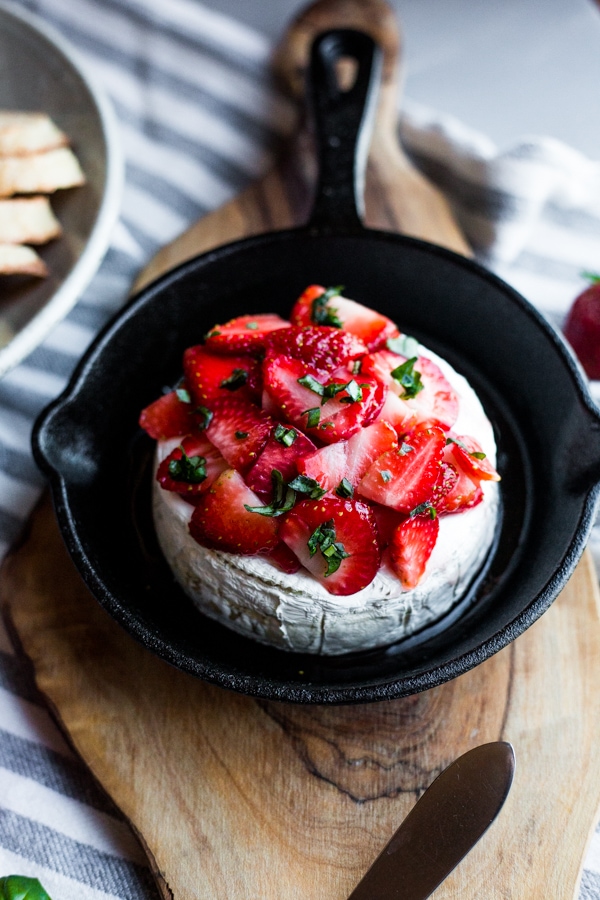 A cast iron skillet with a wheel of brie topped with honey glazed strawberries