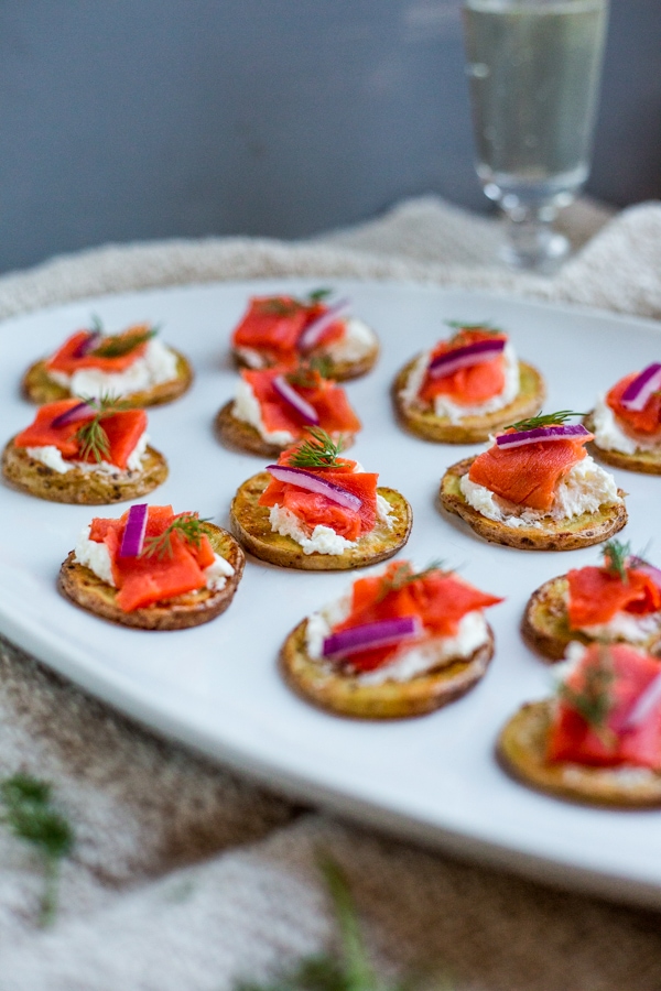 A plate topped with roasted potato slices that are topped with whipped cream cheese, smoked salmon, red onion, and dill