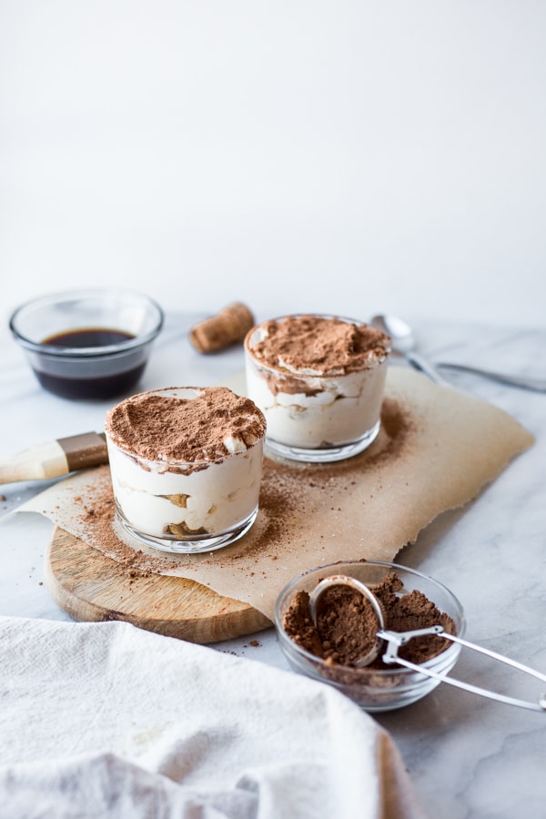 Two dishes filled with tiramisu with a small mesh strainer filled with cocoa powder